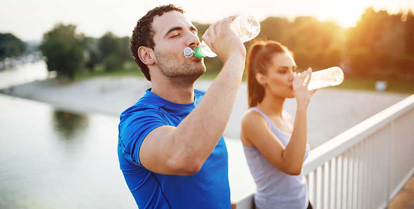 man and woman drinking a bottle of water after working out